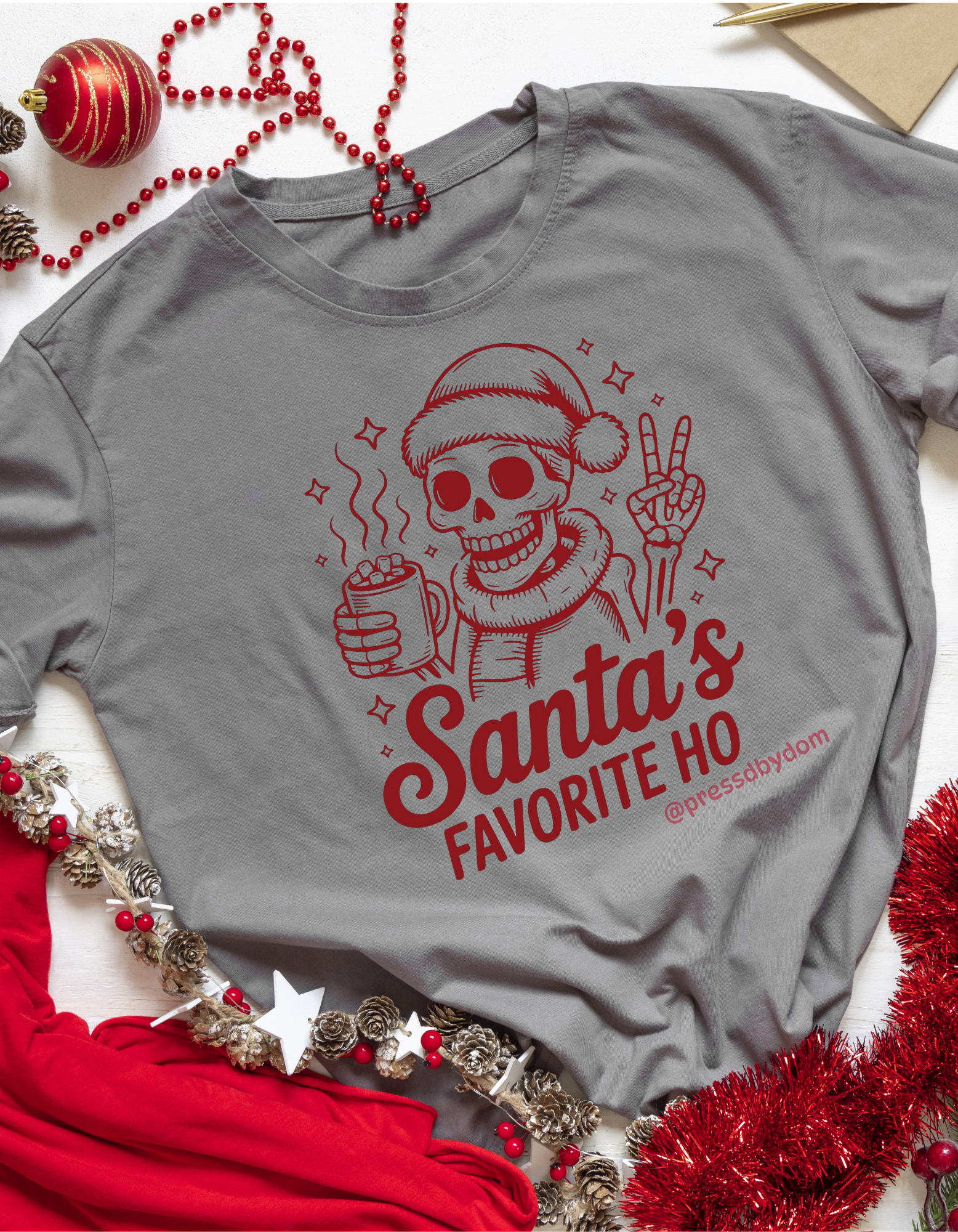 Gray shirt with red skeleton design and 'Santa's Favorite Ho' text, surrounded by Christmas decorations.